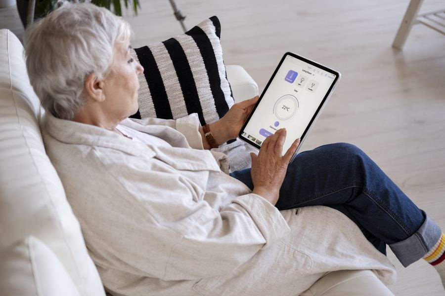 An older adult adjusting their home settings on a tablet from the sofa.